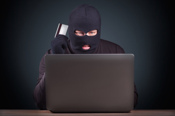 Hacker holding a credit card on wooden background