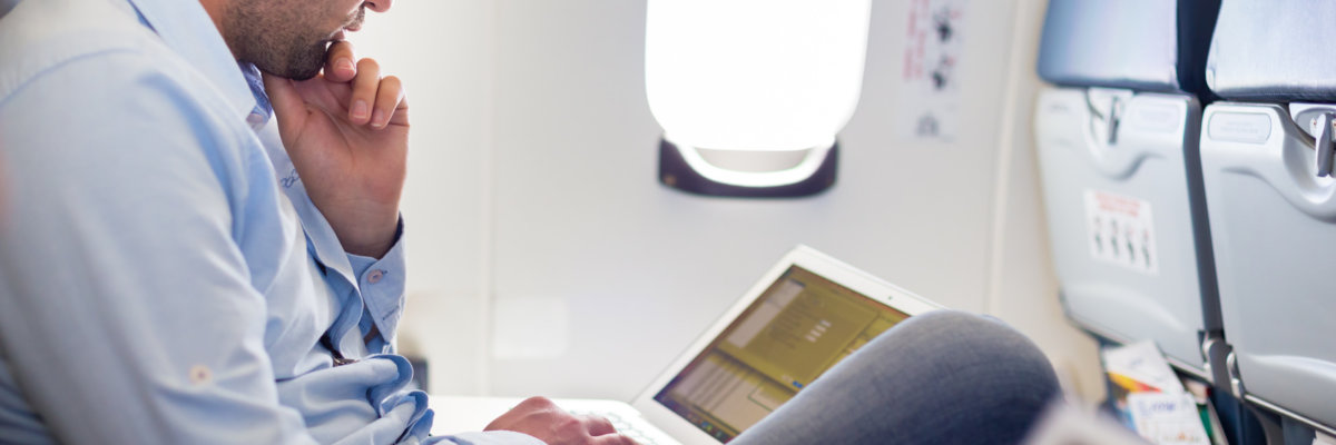 Casually dressed middle aged man working on laptop in aircraft cabin during his business travel. Shallow depth of field photo with focus on businessman eye.